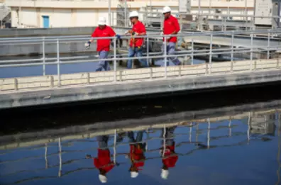 Three men from the staff, wearing uniforms and helmets, walking in our municipal waste water treatment plant